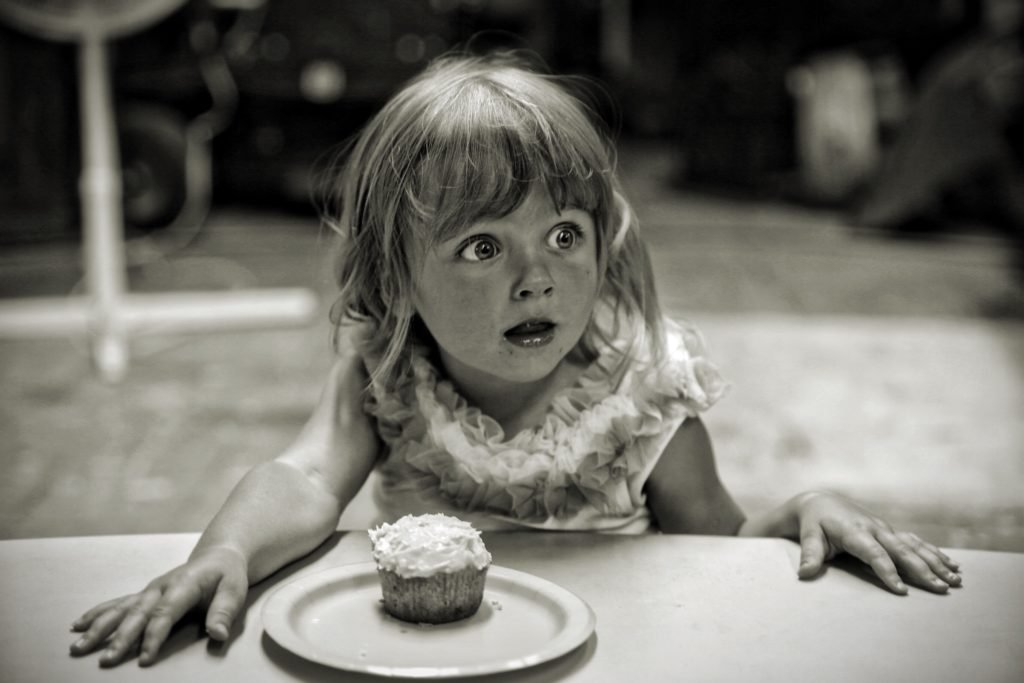 Une petite fille est surprise et devant elle sur une table est posée une assiette avec un gâteau.